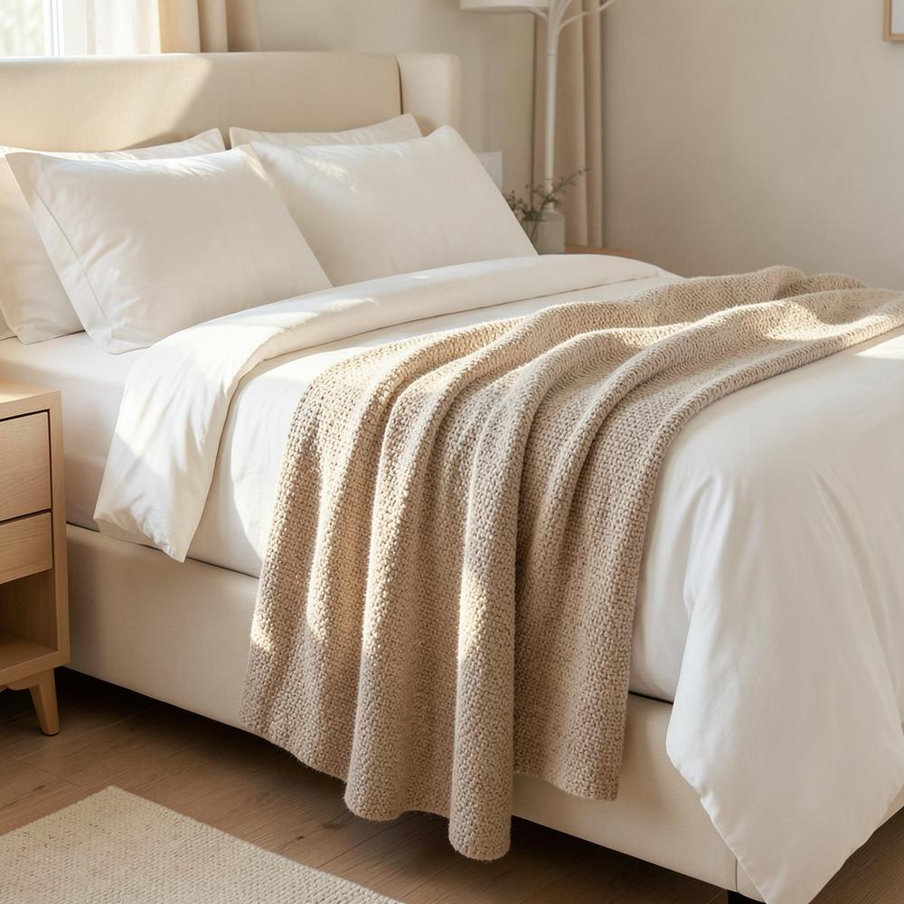 Beige woven winter blanket across the foot of an ivory bed